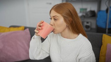 Genç, kızıl saçlı bir kadın sıcak, modern bir apartman dairesinde çay içiyor..