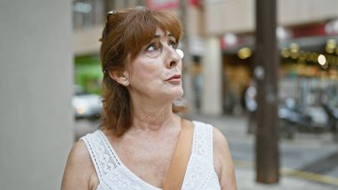 Olgun kızıl saçlı kadın hareketli bir şehir caddesinde dalgın dalgın dalgın dalgın dalgın, şehir hayatını somutlaştırıyor..