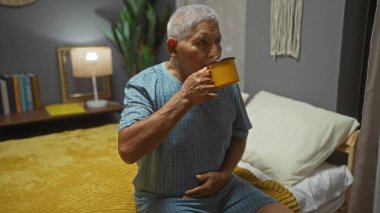 Sarı bardaktan içen, rahat bir yatak odasında oturan, beyaz saçlı İspanyol bir son sınıf öğrencisi..