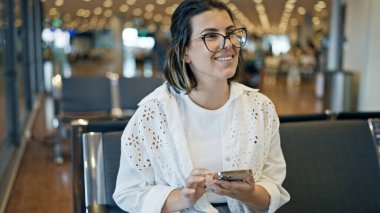 Havaalanında gülümseyen akıllı telefon kullanan güzel bir İspanyol kadın.