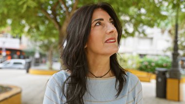 İspanyol son sınıf öğrencisi kadın şehirdeki yeşil yemyeşil bir parkta düşünceli görünüyor..