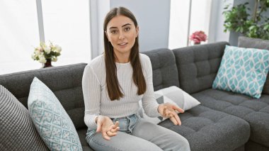 Genç bir İspanyol kadın, güzel dekore edilmiş bir oturma odasında rahat bir koltukta oturmuş, modern ev dekorasyonlarını somutlaştırıyor..