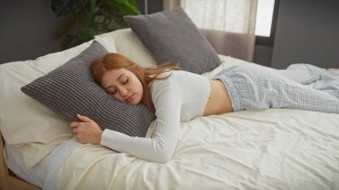 Genç, kızıl saçlı bir kadın yatak odasında huzur içinde uyuyor. Huzurlu, güzel ve rahat bir ev atmosferi yaratıyor..