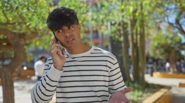 Güneşli bir günde, şehir parkında genç bir İspanyol telefonda konuşuyor..