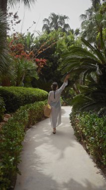 Bir kadın yemyeşil bir bali tatil köyünde dolaşır, gevşeme ve tropikal zarafeti somutlaştırır..