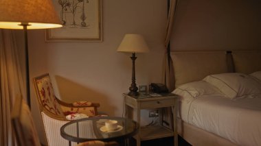 Sıcak ışıklandırması, rahat yatağı, klasik koltuğu ve dekoratif sanat eserleri olan rahat bir otel odası..