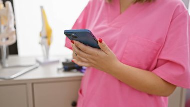 Pembe önlüklü İspanyol bir kadın klinikte akıllı telefon kullanıyor. Sağlık görevlilerini temsil ediyor..