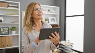 Modern ofiste tablet kullanan sarışın kadın, iş ortamında profesyonellik ve teknoloji taşıyor..