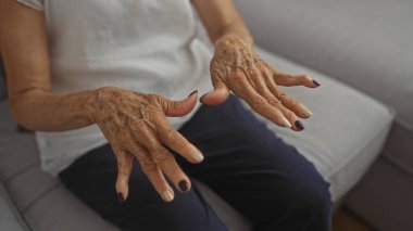 Yaşlı bir kadın olgun ellerini evin içinde sergiliyor oturma odasında otururken boyalı tırnaklarıyla kişisel tarzını sergiliyor..