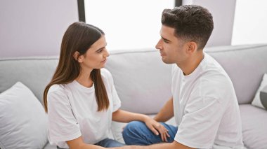 Bir adam ve bir kadın kanepeye yakın oturuyor, modern bir oturma odasında sevgi dolu bir sohbete girişiyor..