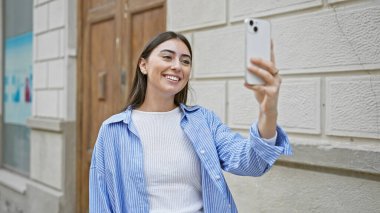 Mutlu genç İspanyol kadın akıllı telefonuyla şehirde selfie çekiyor..