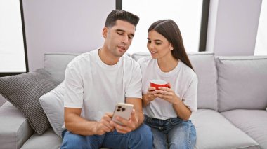 Sevgi dolu bir çift, evde rahat bir anın tadını çıkarır. Elinde akıllı telefon tutan adam ve elinde kırmızı kupa tutan kadın..