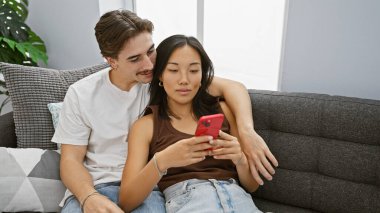 Irklar arası bir çift, oturma odasında akıllı telefonlara bakan bir kadın ve bir erkekle birlikte eğleniyor.