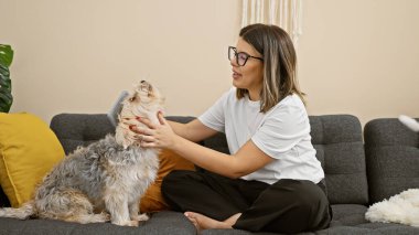 İspanyol kadın, sıcak bir oturma odasındaki kanepede sevimli bir köpeği tımar ediyor..