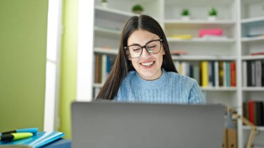 Kütüphanede gülümseyen dizüstü bilgisayar kullanan İspanyol bir kız öğrenci.