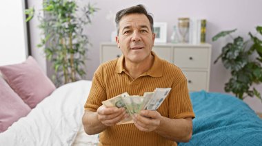 Mature man counting singapore dollars in a cozy bedroom interior, reflecting retirement savings or budgeting. clipart