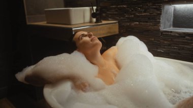 Genç bir İspanyol kadın modern bir banyoda köpüklü bir banyoda dinleniyor..