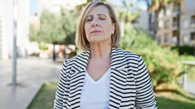 Sakin sarışın bir kadın yeşil bir şehir parkında huzurlu bir anın tadını çıkarıyor..