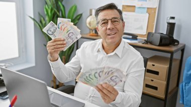 Orta yaşlı bir adam modern bir ofiste tek başına para tutuyor, başarılı bir iş ortamını canlandırıyor..
