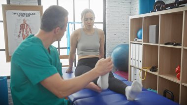 Bir kadın hasta, erkek bir fizyoterapistle birlikte kapalı bir klinikte bacak rehabilitasyonundan geçiyor..