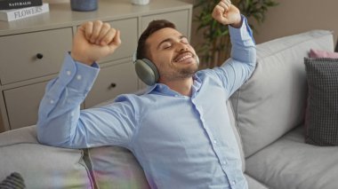 Yakışıklı, sakallı, oturma odasındaki kanepede dinlenirken kulaklıkla müzik dinleyen bir İspanyol..