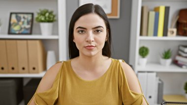 Kendine güvenen genç bir İspanyol kadın modern ofis ortamında poz veriyor, profesyonellik ve duruş sergiliyor..