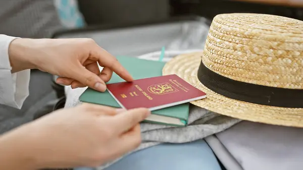 Stock image Close-up of a female hand placing a finnish passport into a suitcase next to a straw hat, indoors.