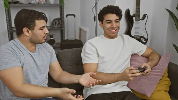 stock image Two hispanic men enjoying video games in a cozy living room with a guitar in the background