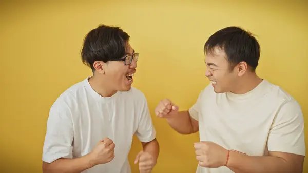 stock image Two asian men laughing together against a yellow background, portraying friendship and joy.