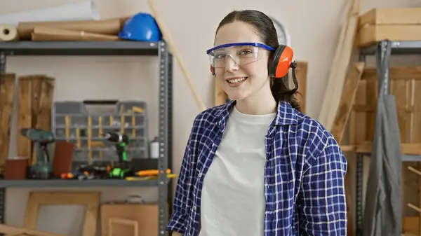 stock image Smiling woman in safety gear posing in a carpentry workshop.