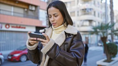 Meşgul bir şehir sokağında akıllı telefon kullanan genç bir İspanyol kadın.