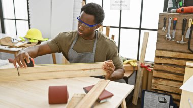 İyi donanımlı bir marangozluk atölyesinde odun ölçen Afrikalı Amerikalı bir adam.