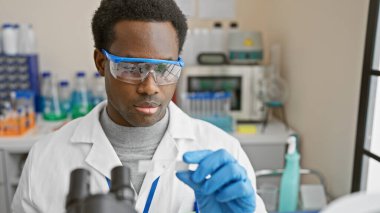 Afrika kökenli Amerikalı erkek bilim adamı bir laboratuvar ortamında araştırma ve sağlık hizmetlerini canlandıran bir örneği analiz ediyor..