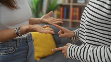 Two women gesturing in a conversation in a cozy living room, conveying friendship and communication. clipart