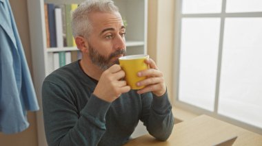 Düşünceli, olgun, sakallı bir adam evde kahvenin tadını çıkarıyor..