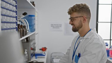 Laboratuar önlüklü, sakallı ve gözlüklü gülümseyen beyaz adam bir eczanede ya da kapalı bir laboratuarda duruyor..