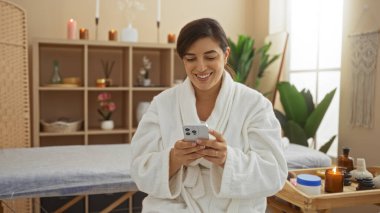 Kaplıca odasında gülümseyen bir kadın. Etrafı çiçeklerle, mumlarla ve yağlarla çevrili beyaz bornozla çevrili..