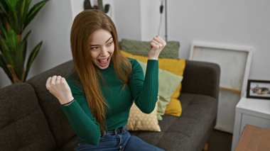 Heyecanlı, genç, beyaz bir kadın sıcak bir oturma odasında kutlama yapıyor..