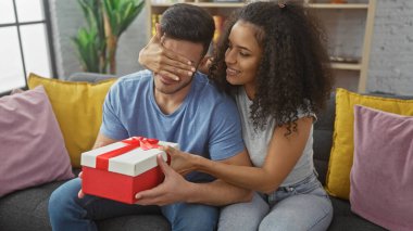 Bir kadın, güzel bir oturma odasında hediyesiyle bir erkeği şaşırtır. Aşkı ve kutlamayı sembolize eder..