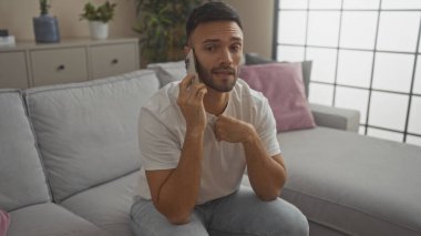 Evinin oturma odasında otururken cep telefonuyla konuşan sakallı yakışıklı İspanyol bir adam..