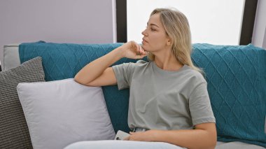 Kanepede oturan düşünceli bir kadın, rahat bir eve bakıyor..