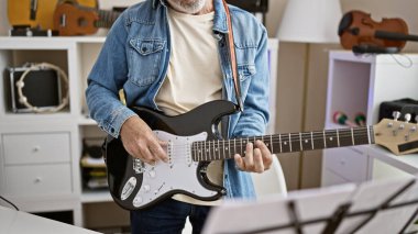 Gündelik kıyafetli olgun bir adam müzik aletleriyle dolu modern bir odada elektro gitar çalar..