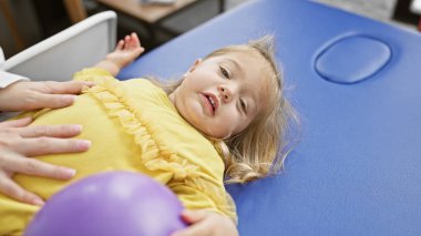 Blonde girl undergoing physiotherapy treatment in a clinic with female therapist clipart