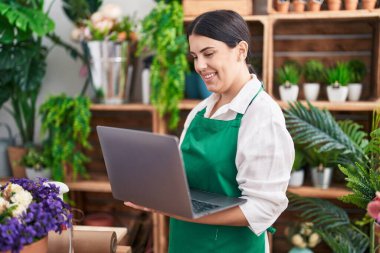 Young beautiful hispanic woman florist smiling confident using laptop at flower shop