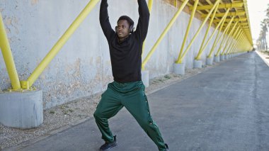 Gündelik giysiler içinde genç bir Afrikalı Amerikalı güneşli bir caddede kulaklık takarken esniyor..