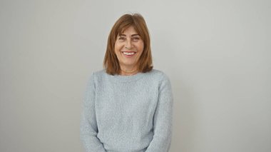 Gülümseyen orta yaşlı bir kadın, kısa saçlı, beyaz arka planda günlük kıyafetler giyiyor..