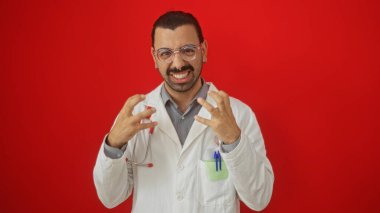 Beyaz önlüklü, bıyıklı genç İspanyol bir adam izole edilmiş kırmızı bir arka plana kızgınlığını dile getiriyor.