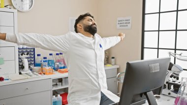 Etrafında bilimsel ekipmanlarla bir laboratuvar ortamında gerinen İspanyol bir adam..