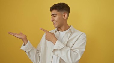 Sarı izole edilmiş bir arka planda elleri olan gülümseyen genç bir adam, dost canlısı ve kendinden emin bir atmosferi çağrıştırıyor..