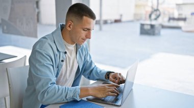 Üniversite kütüphanesinde dizüstü bilgisayar kullanan genç İspanyol, öğrenci portresi, eğitim, kapalı alan, günlük çalışma, odaklanma, teknoloji, yetişkin, erkek.